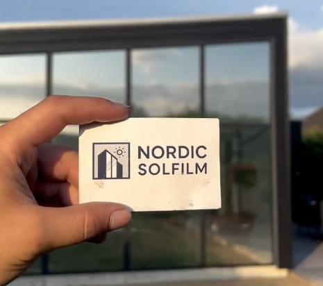 Nordic Solfilm visitkort holdt foran glasparti med monteret solfilm